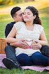 Pregnant Hispanic Couple Making Heart Shape with Hands on Belly in The Park Outdoors.