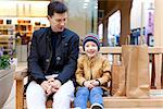 family of young father and excited son sitting on the bench in shopping mall