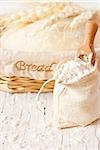 Bag of flour with wooden scoop and fresh homemade dough for bread in a basket on an old white kitchen board.