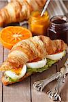 Fresh croissant with boiled egg and salad and salad, sweet jam and orange fruit for breakfast on a wooden board close-up.