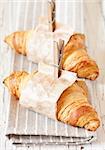 Fresh croissants wrapped in paper with clothespins on an old white board.