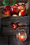 Sweet ripe red apples in an old wooden box and garden jar candle on wooden background.