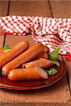 delicious smoked sausages on a wooden plate with basil leaves