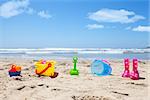 Colorful plastic toys and gumboots on beach sand with sea in background