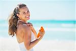 Smiling young woman on beach applying sun block creme