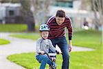 young father teaching his smiling son how to ride a bike