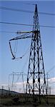 pillars with electricity transmitting lines in field under blue skies