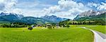 Summer Alpine mountain country panorama with grassy meadow and road to village (Austria)