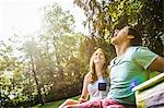 Young man trying to catch grape in his mouth, sitting with girlfriend in park