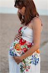 Side view of pregnant woman, hands on stomach, looking down