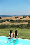 Teenage girls in swimming pool looking at view of Tuscany, Italy
