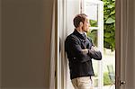 Mid adult man looking out of window, arms folded