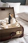 Open suitcase on bed with wedding figurines