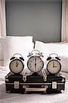 Closed suitcase on bed with three alarm clocks