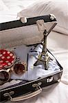 Open suitcase on bed with eiffel tower souvenir and sunglasses