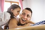 Young man and daughter on bed in holiday chalet, Tyrol, Austria