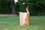 Young boy watching from cardboard box in garden