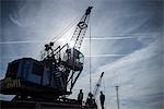 Low angle view of workers and crane in silhouette in port