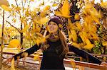 Young woman throwing up autumn leaves in park