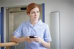 Female nurse with mobile phone outside hospital lift