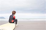 Boy sitting on surfboard on beach