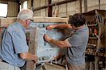 Father watching son restore boat in workshop