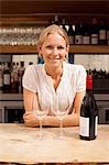 Portrait of waitress with wine bottle and glasses at kitchen counter