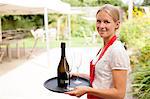 Portrait of waitress with tray of wine and glasses in cafe garden