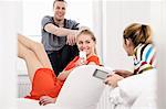 Three young adult friends with mobiles and digital tablet in bedroom