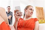 Young adult couple lounging in sitting room with mobile