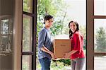 Young couple carrying cardboard box into new house