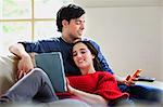 Young couple with digital tablet and mobile on living room sofa