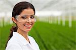 Scientist wearing goggles in front of plants in greenhouse