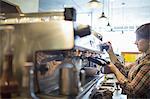 A person, barista making coffee, and frothing milk using a steam pipe, for a cappuccino. Coffee shop.