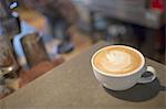 Coffee shop table. A full white china cup of coffee with a frothed milk top.