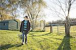 A young boy in an animal paddock, holding a bucket of feed. Animal sanctuary.