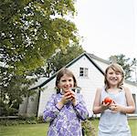 Two children, girls standing in a garden holding and eating fresh picked tomatoes.