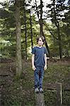 A boy standing on a narrow tree trunk, balancing and walking the plank.