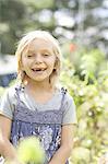 A young girl sitting in among the fresh green foliage of a garden. Vegetables and flowers. Picking fresh vegetables.