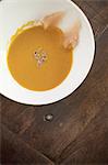 A white china bowl with a creamy soup and garnish, viewed from above. A rouille puree on the side of the dish.