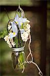 A small glass jar hanging from a wire, with iris and scented stock flowers. A floral decoration.