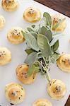 Organic dinner bread rolls on a white board with salt and sage garnish