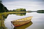 A small wooden dory or rowing boat moored on flat calm water, in Savage harbour on Prince Edward Island in Canada.