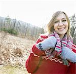 A woman wearing a knitted scarf and woollen mittens outdoors on a winter day.