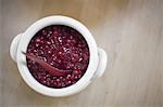 A white pottery bowl, full of fresh cranberries with a matching spoon. A relish or sauce.