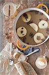 Overhead view of a kitchen table. A large cooking pan with double handles. Sliced cored apples, cloves and star anise with cinnamon. Making a mulled fruit drink.