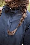 A woman with long brown hair plaited in a braid. Wearing a blue leather jacket. Close up.