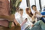 Urban Lifestyle. A group of people, men and women on a city bus, in New York city. Two people checking their phones. One man standing holding a bunch of flowers.