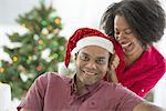 A man in a Father Christmas hat. At home. A decorated Christmas tree.