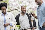 Three people in the park. One man checking his phone.